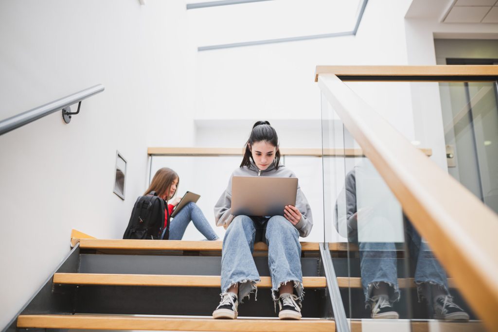 Foto van een studente op de trap van een schoolgebouw. Sfeerbeeld bij een intro voor een case over Koers VO, een samenwerkingsverband in de regio Rotterdam.